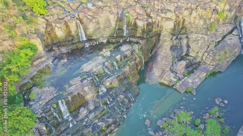 Drone Shows Blue Pond with Waterfall Cascade among Rocks photo