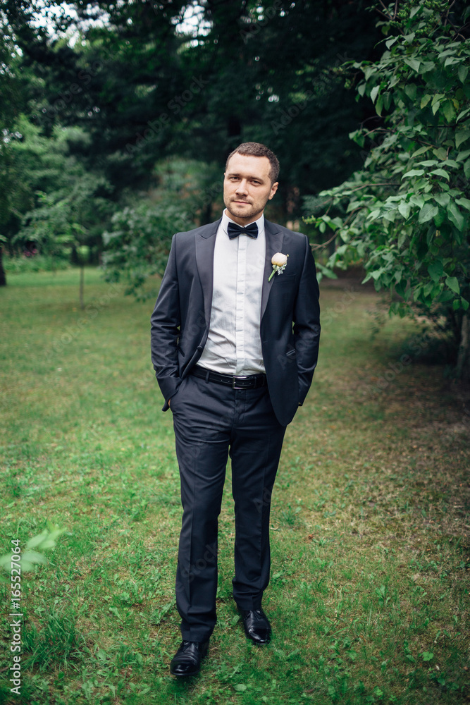 Groom in black tuxedo walks on the backyard Groom in black tuxedo walks on the backyard