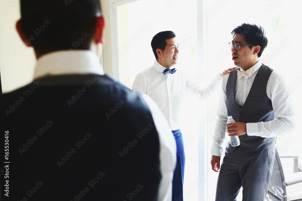 Groom and groomsmen talk standing before a bright window in the room Groom and groomsmen talk standing before a bright window in the room