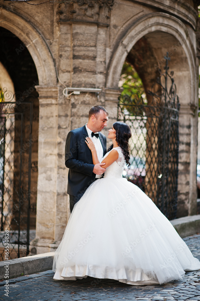 Amazing young attractive newly married couple walking and posing in the downtown with beautiful and ancient architecture on the background on their wedding day.