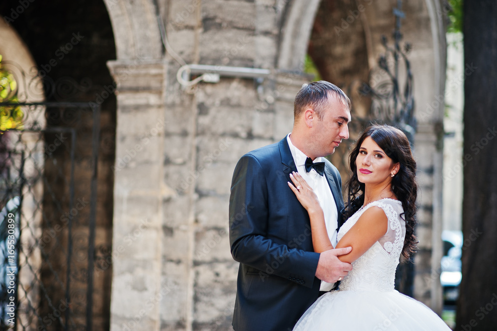 Amazing young attractive newly married couple walking and posing in the downtown with beautiful and ancient architecture on the background on their wedding day. Amazing young attractive newly married couple walking and posing in the downtown with beautiful and ancient architecture on the background on their wedding day.