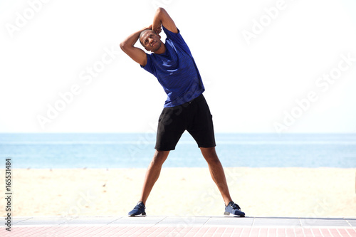 Full length healthy black man stretching in morning on beach