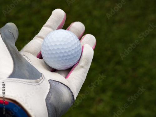 Golfer hand wearing golfer glove and holding golf ball on fairway grass in golf course