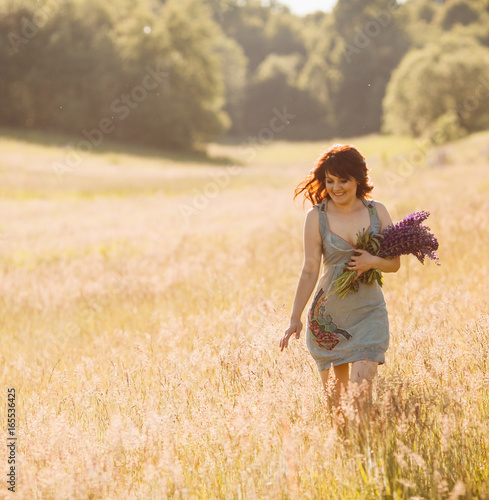 Woman walks with bouquet of lavander across the field