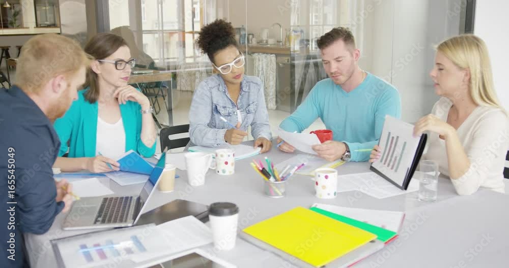 Side view of woman holding folder with document and showing it to coworkers while having conference at table in modern office. Side view of woman holding folder with document and showing it to coworkers while having conference at table in modern office.