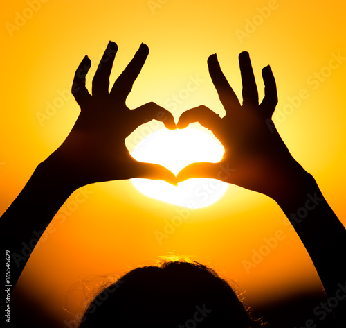 Silhouette of the heart by hands at sunset