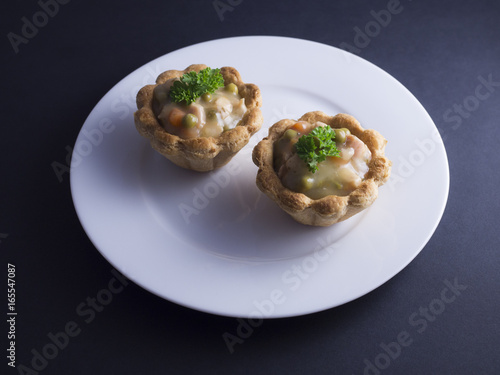 Savory Danish tartlets (tarteletter) made from puff pastry, filled with a creamy chicken, asparagus and carrot sauce. Placed on white plate and isolated on black background