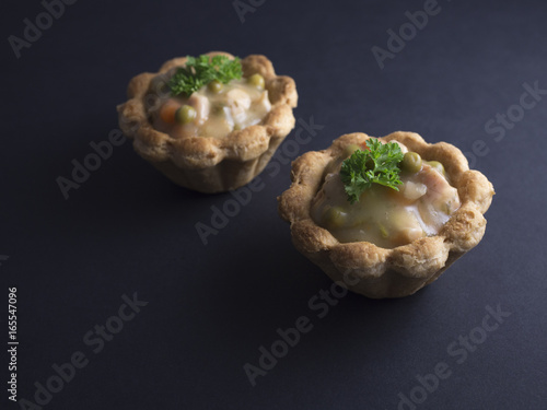 Savory Danish tartlets (tarteletter) made from puff pastry, filled with a creamy chicken, asparagus and carrot sauce. Isolated on black background