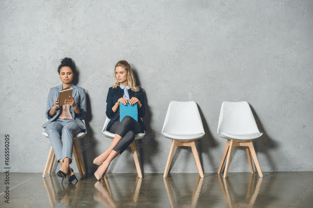 young multicultural businesswomen sitting on chairs and waiting for job interview young multicultural businesswomen sitting on chairs and waiting for job interview