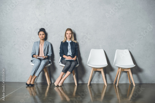 young multicultural businesswomen sitting on chairs and waiting for job interview