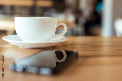 selective focus of cup of coffee on saucer standing on wooden table in cafe