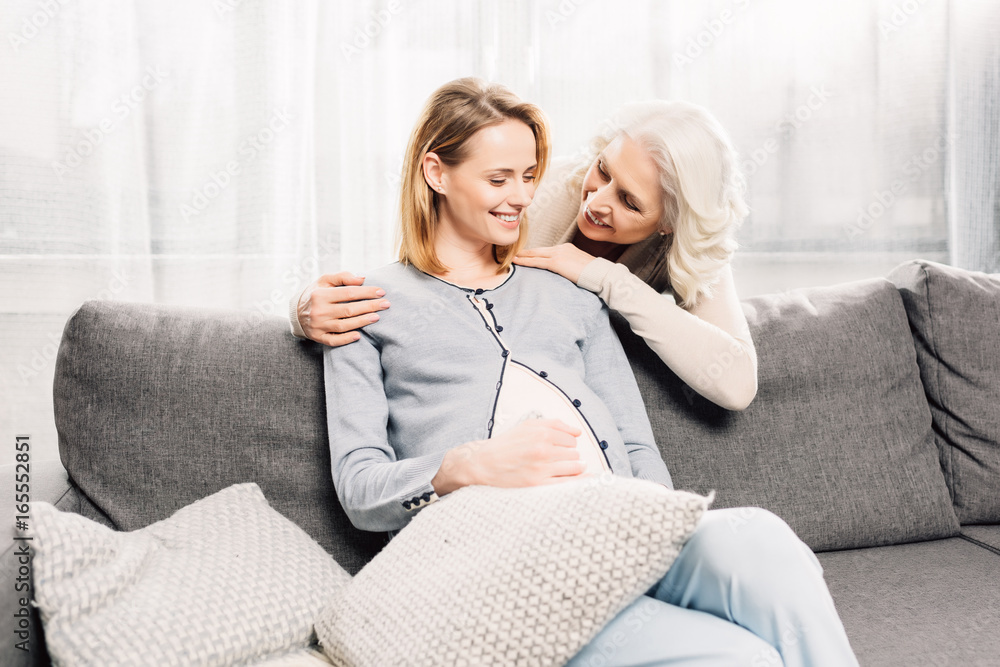 Young pregnant woman on gray sofa with her mother in room Young pregnant woman on gray sofa with her mother in room