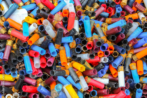 Many shotgun shells of various colors, background texture pattern with empty fired cartridges.