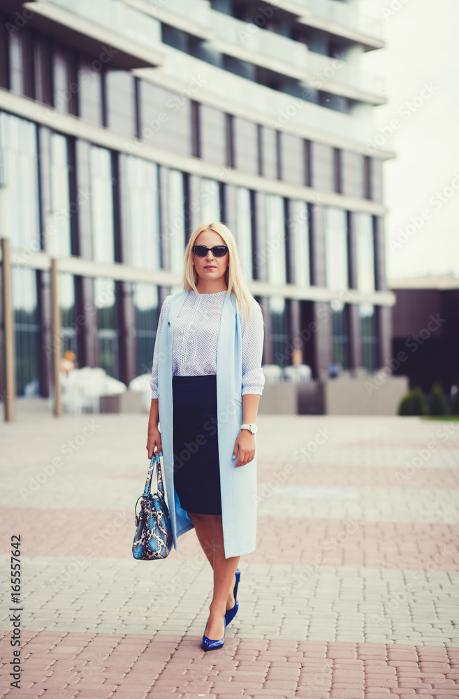 Business lady in a blue coat near an office building with a bag