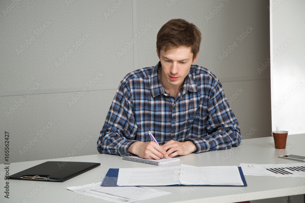 worker is carefully studying the job, which is received from the head, man looks at documents and write notes in your notebook worker is carefully studying the job, which is received from the head, man looks at documents and write notes in your notebook