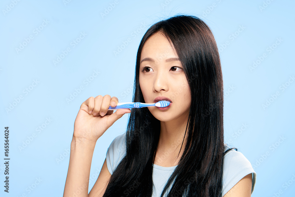 Beautiful young woman on a blue background brushes teeth, asian Beautiful young woman on a blue background brushes teeth, asian