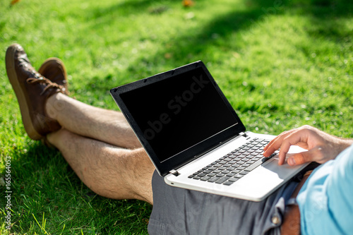 Cropped shot of man using laptop with blank screen while sitting on green grass photo