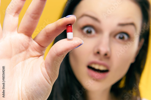 Beautiful young woman on a yellow background holds a pill, pharmacy, medicine