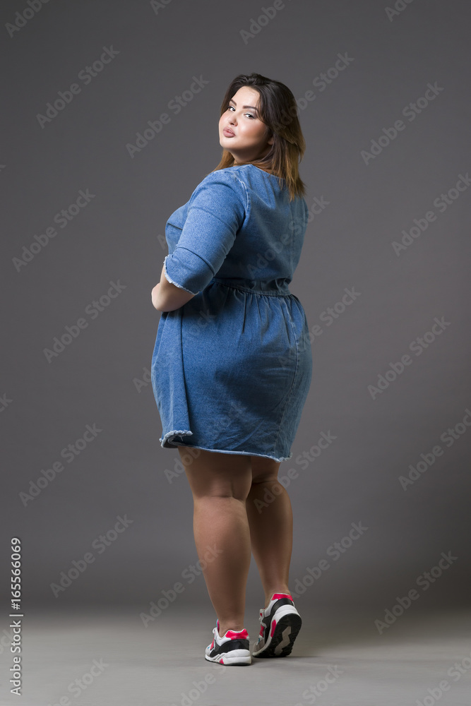 Plus size model in denim dress, fat woman on gray background, wall