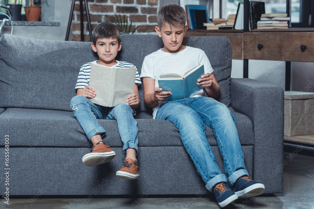 little caucasian boys reading books while sitting on sofa at home little caucasian boys reading books while sitting on sofa at home