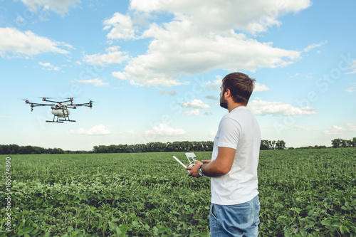 Young man operating of flying drone octocopter at the green field. Professional agriculture drone flying with blue sky.
