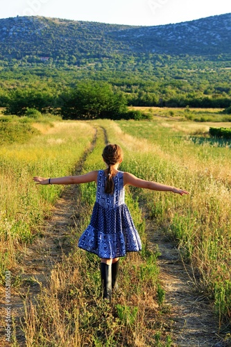 rückenansicht eines mädchensin kleid und stiefel, spuren in der wiese folgend/gras, feld, landschaft, unbeschwerte kindheit am land