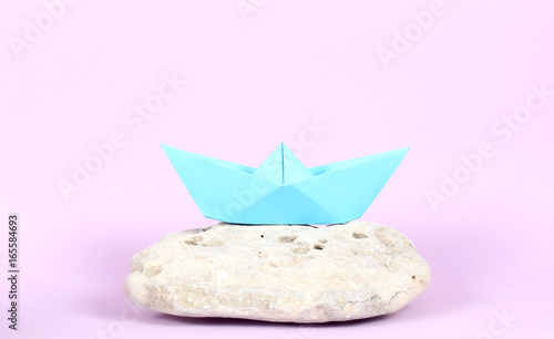 кораблик из бумаги голубого цвета стоит на камнях 