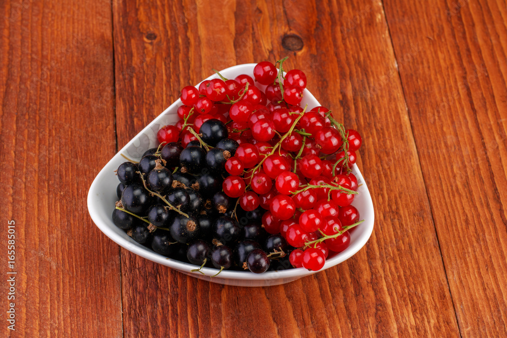 Red and black currants in ceramic bowl on wood background Red and black currants in ceramic bowl on wood background