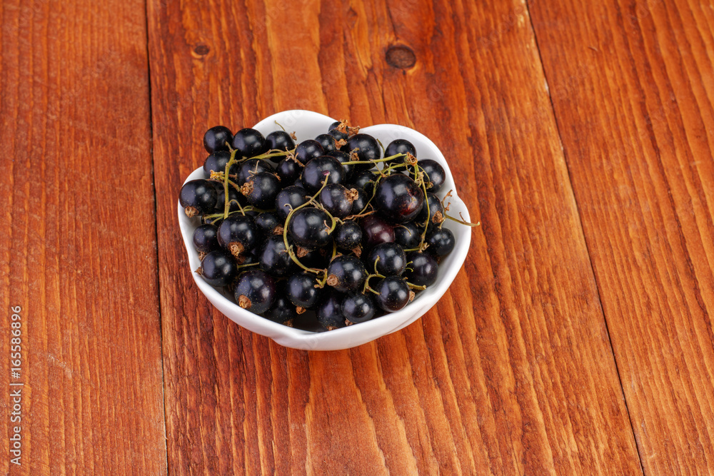 Black currants in ceramic bowl on wood background Black currants in ceramic bowl on wood background