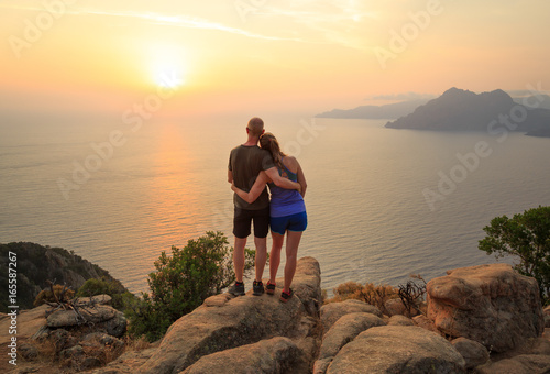 Outdoor couple enjoying the sunset over the Golf of Porto at the famous Chateau Fort. Corsica, France.