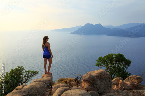Young woman looking over the sea from the rocks near the famous Chateau Fort. Corsica, France.