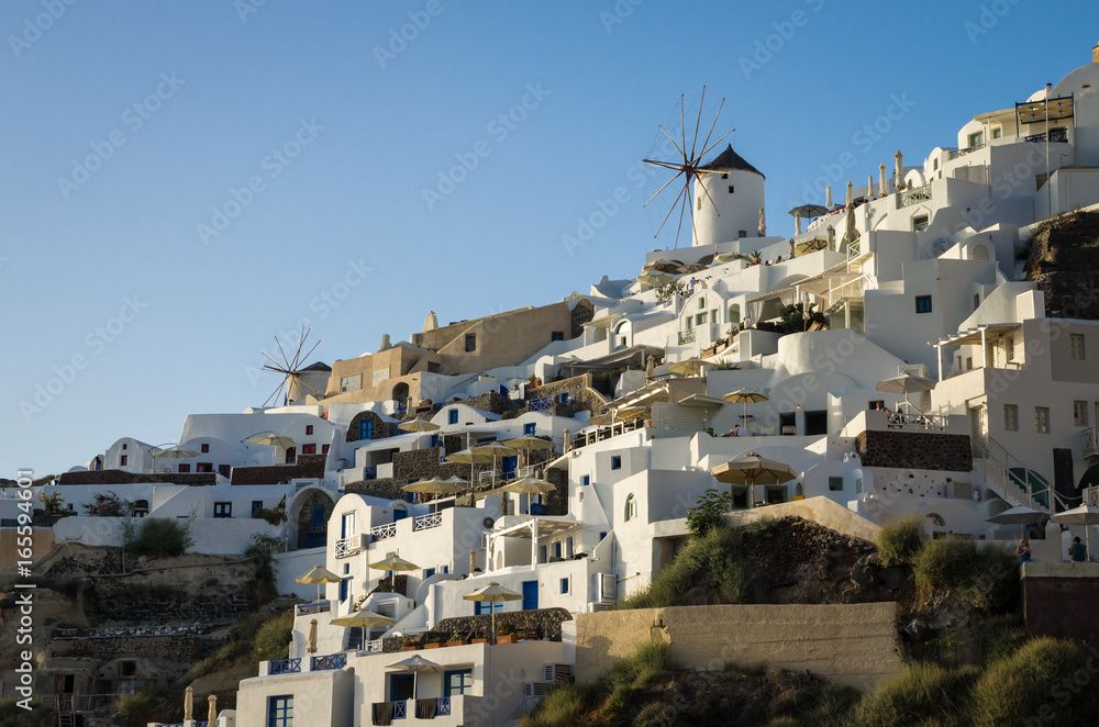 Oia Village, Santorini Cyclade islands, Greece. Beautiful view of the town with white buildings, blue church's roofs and many colored flowers.