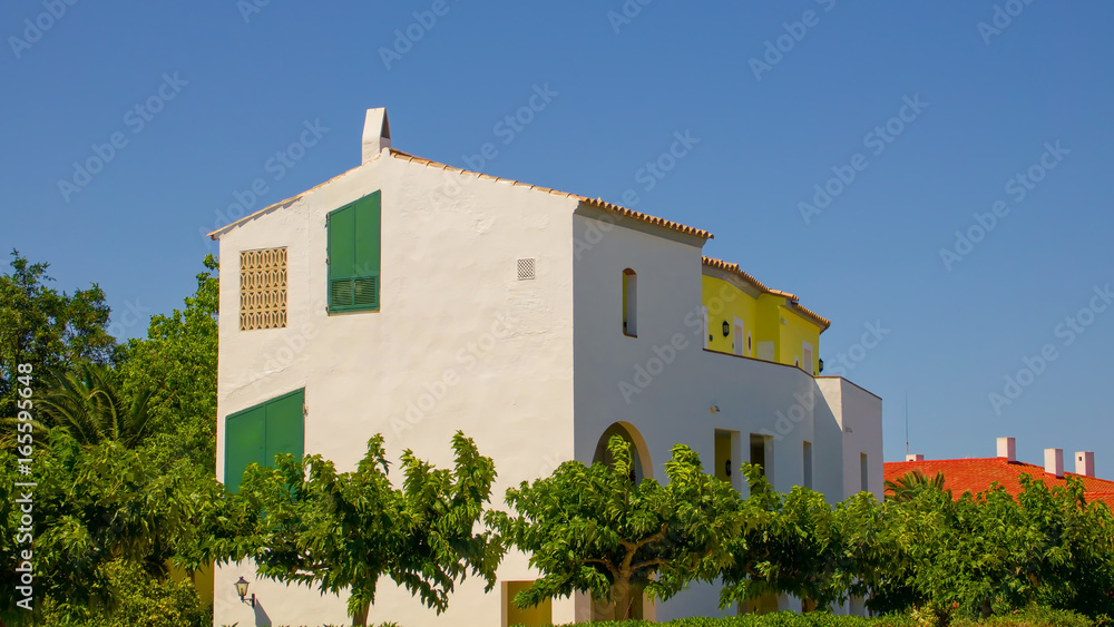 Houses on the island of Menorca in Spain with green shutters, yellow walls and yellow and orange tiled roofs.