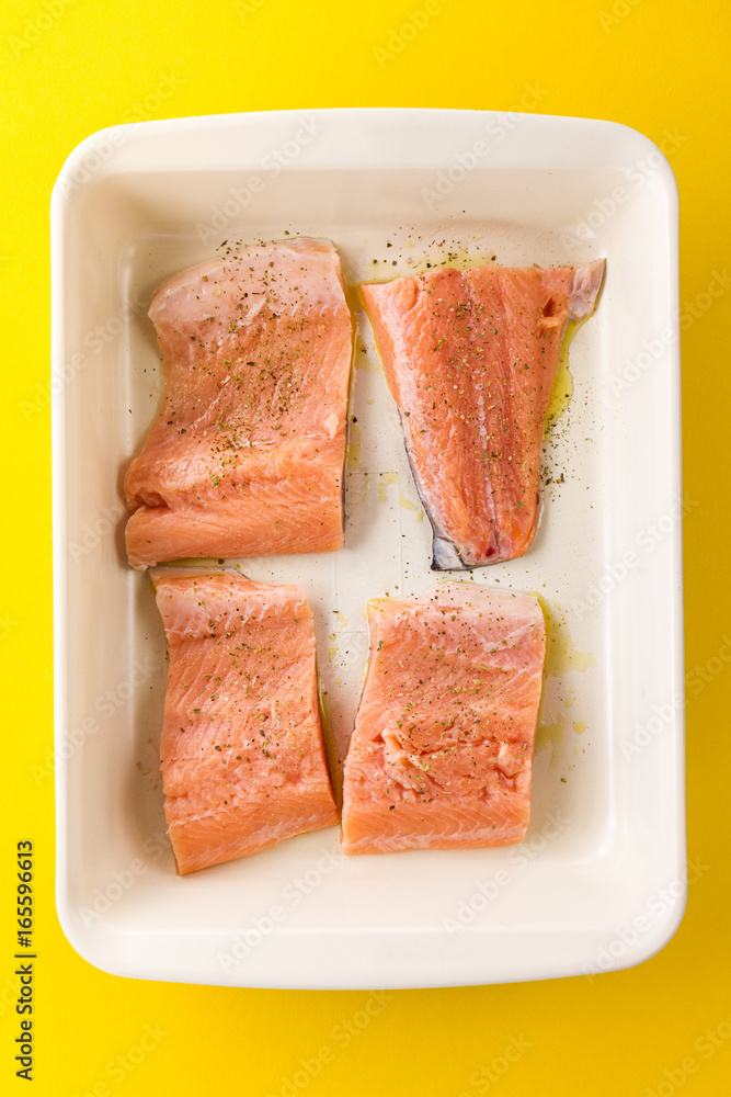 Fresh tasty raw salmon slices in baking form ready to bake on yellow vibrant background. Top View.