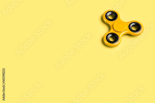 Yellow fidget spinner background template with copy space. Popular kids stress and anxiety relief toy in the top right corner.