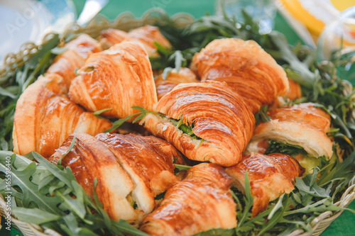 Appetizing croissants with meat and cheese filling and arugula in a woven rustic basket.