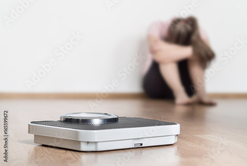 Weight loss fail concept. Scale and depressed, frustrated and sad woman sitting on floor holding head and arms on knees. photo