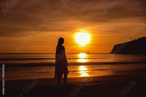 Silhouette of the girl standing at the beach during beautiful sunset. © Ilya