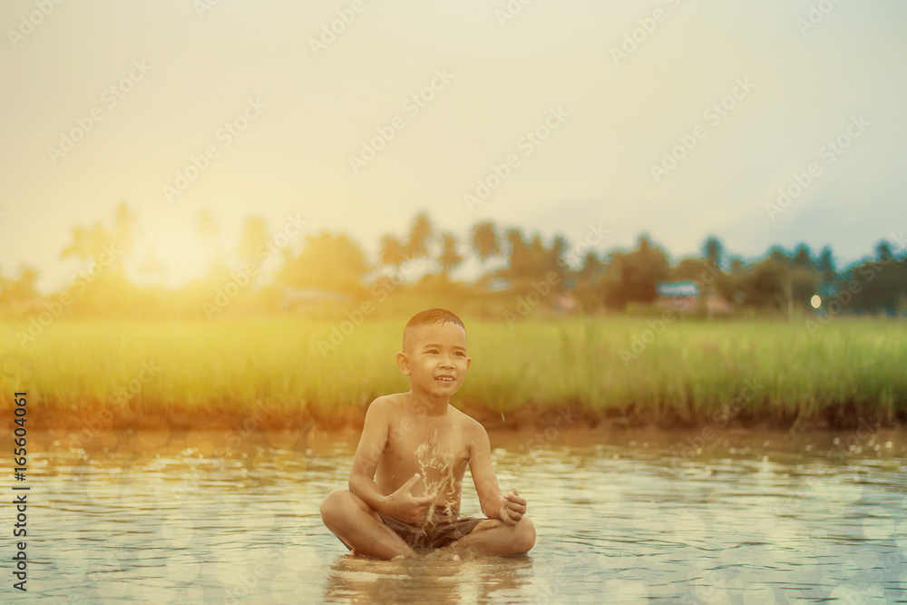 Fototapeta premium Asian Boy playing in water loosen hot looks happy, Before sunset background ,Thailand.