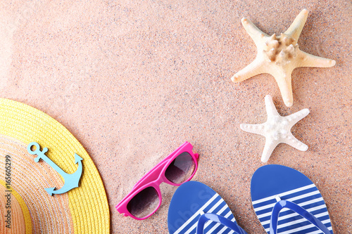 Flip flops with starfish, sunglasses and hat on the beach sand