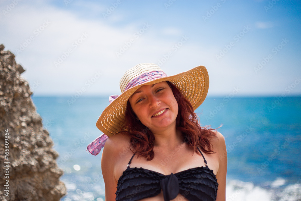 A young girl on the beach, enjoying a holiday in the sun by the sea, a hat on the head, in the background blue sea