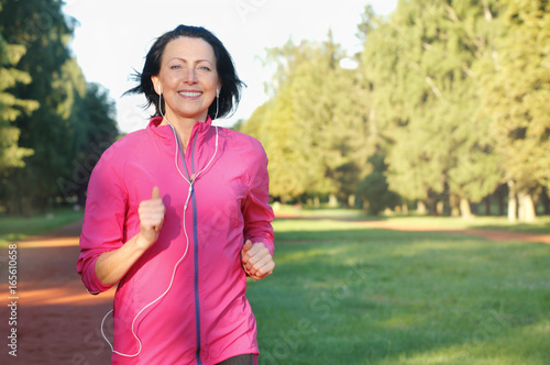 Portrait of elderly woman running with headphones in the park