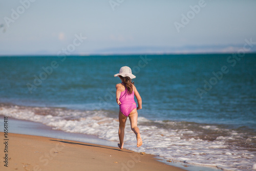 young girl in swimsuit and hat runs along the line of surf on a sandy beach