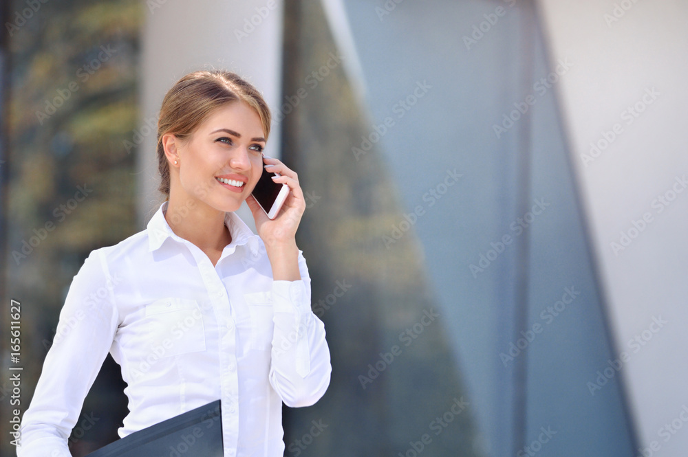Young business woman talking a mobile phone on street against building Young business woman talking a mobile phone on street against building
