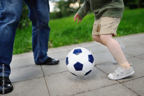 Little boy with his father having fun playing a soccer game on sunny summer day
