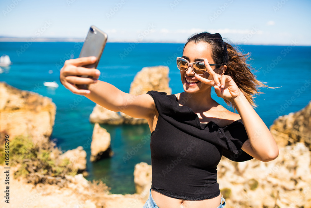 Beauty latin woman take selfie from phone  at the top of beautiful cliff s and rocks of Atlantic ocean in Portugal