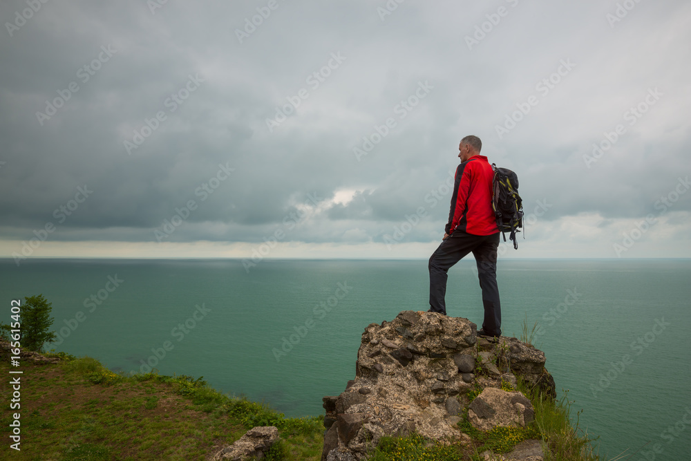 Obraz premium Man traveler stands on a cliff in front of the sea