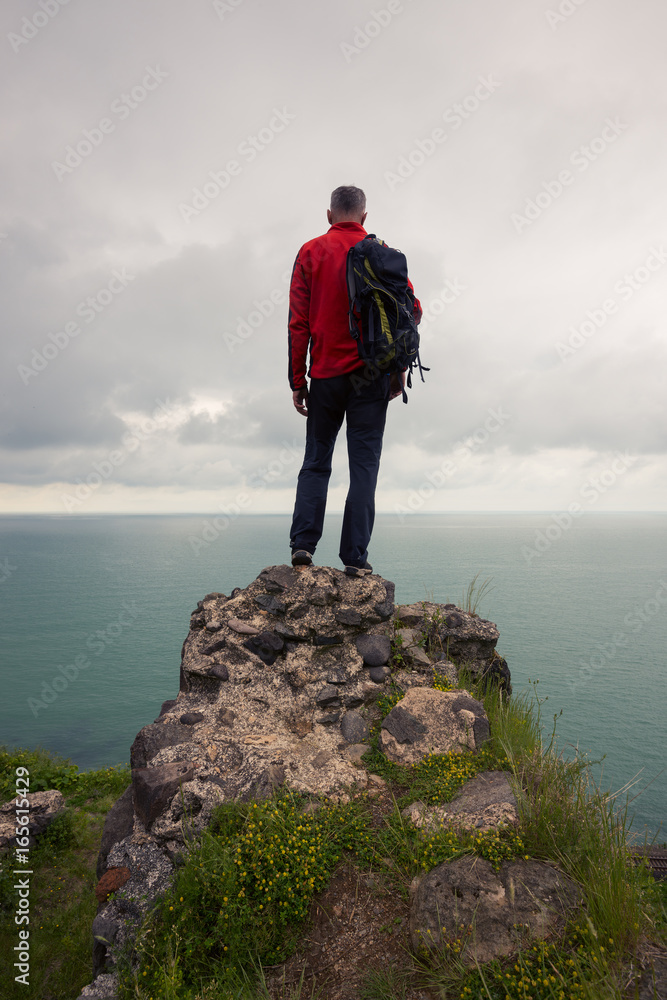 Traveler stands on a cliff and looks at the sea