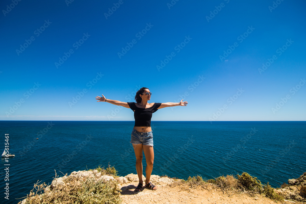 Beautiful latin woman standing on a rock above the ocean and welcomes the summer Beautiful latin woman standing on a rock above the ocean and welcomes the summer