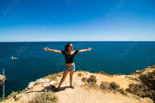 Beautiful latin woman standing on a rock above the ocean and welcomes the summer